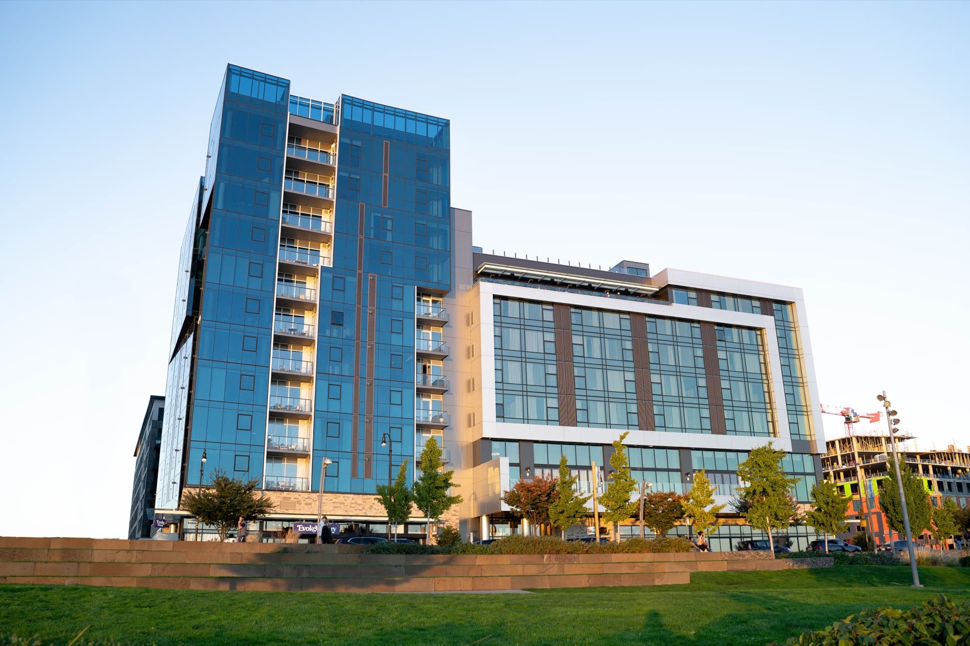 Hotel Indigo Vancouver Waterfront exterior at golden hour, blue glass tower above the public esplanade