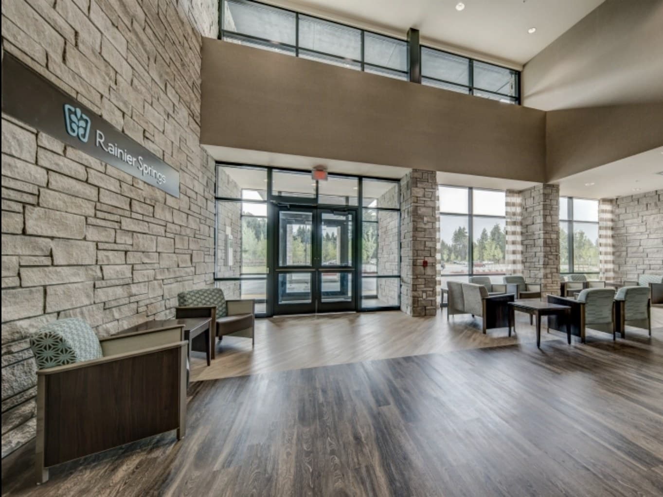 Rainier Springs main lobby, wordmark on stacked-stone wall, double-height ceiling with clerestory windows, glass entry vestibule, Vancouver, Washington